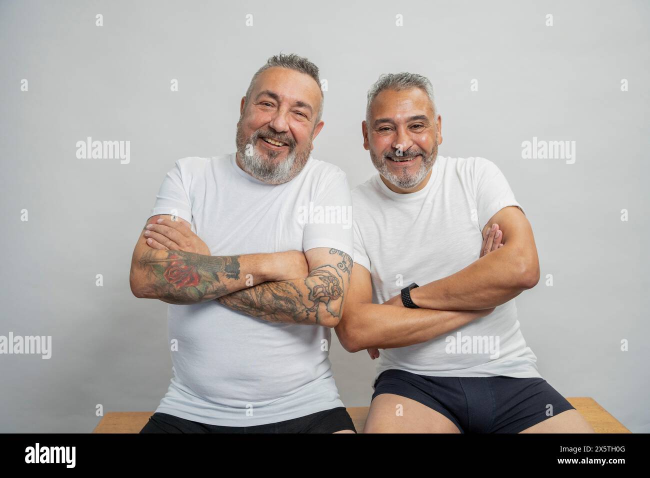 Porträt zweier lächelnder Senioren in weißen T-Shirts vor grauem Hintergrund Stockfoto