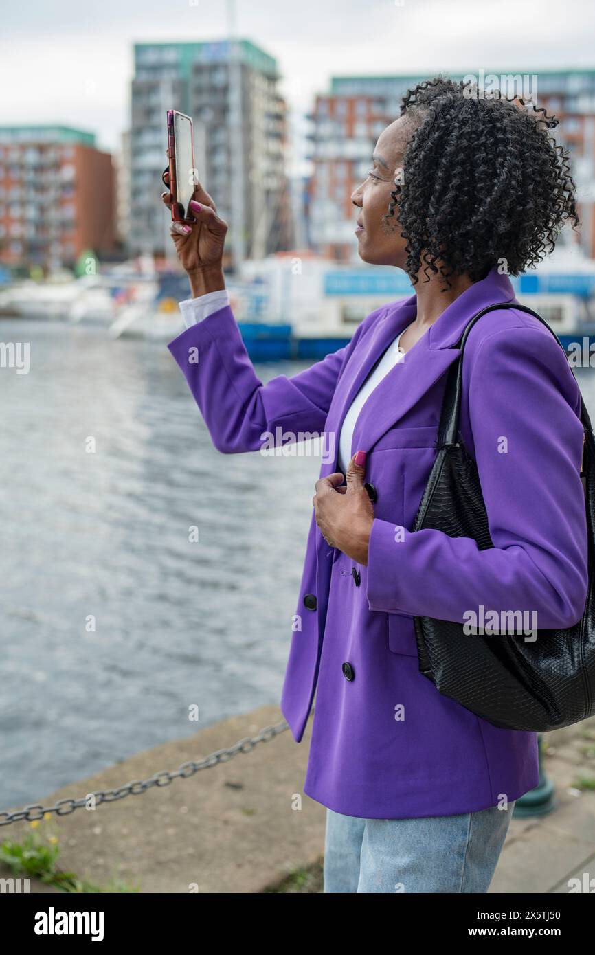 Lächelnde Frau, die mit dem Smartphone den Blick auf die Stadt fotografiert Stockfoto