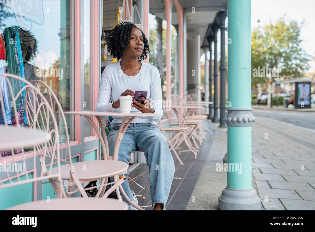 Frau, die ihr Smartphone während der Kaffeepause im Straßencafé benutzt Stockfoto
