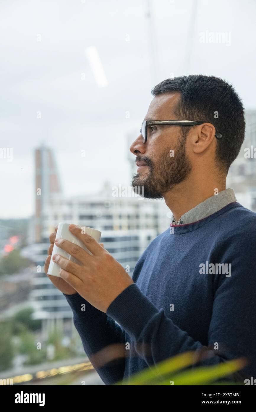 Mann mit Kaffeetasse, der aus dem Fenster blickt Stockfoto