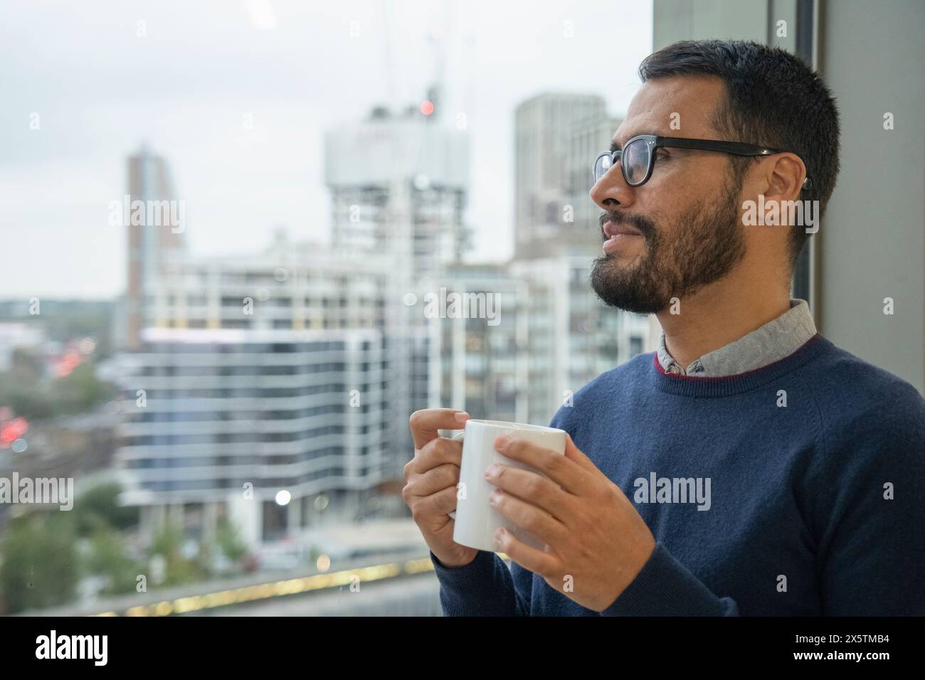 Mann mit Kaffeetasse, der aus dem Fenster blickt Stockfoto