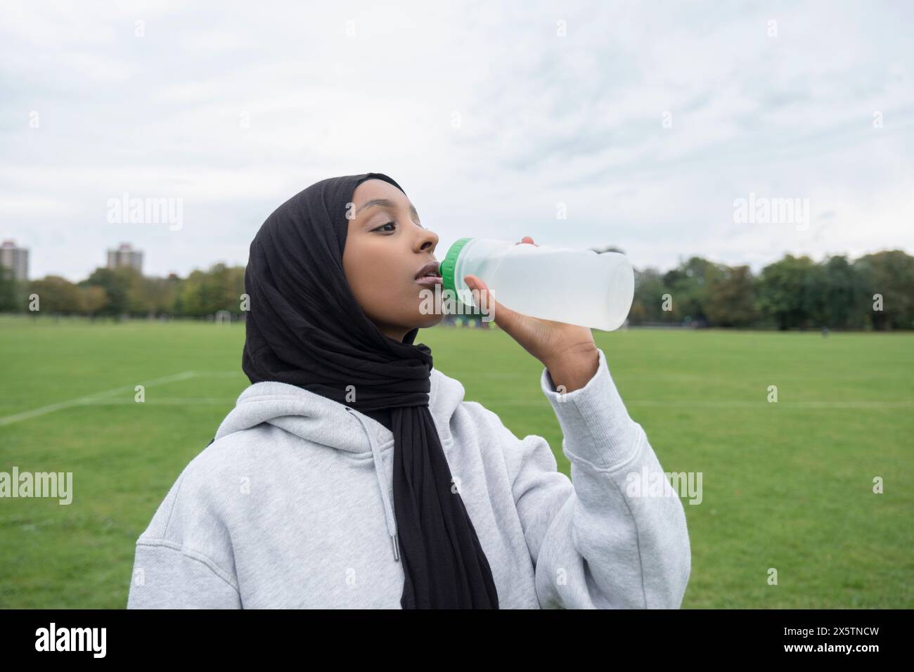 Porträt einer Frau im Hijab-Trinkwasser aus der Flasche auf dem Fußballfeld Stockfoto