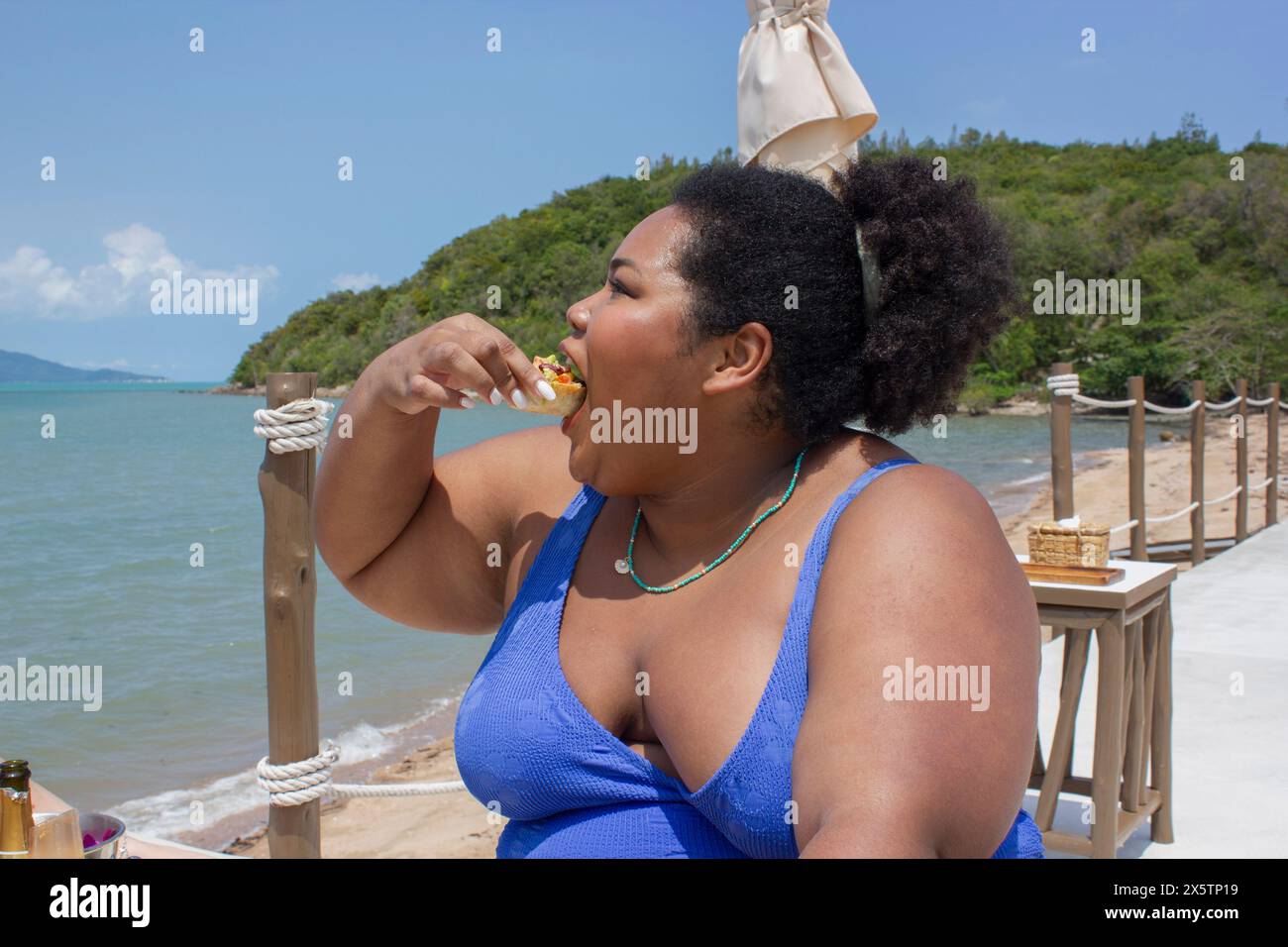 Junge, fröhliche Frau, die beim Picknick in der Nähe der Bucht Essen genießt Stockfoto