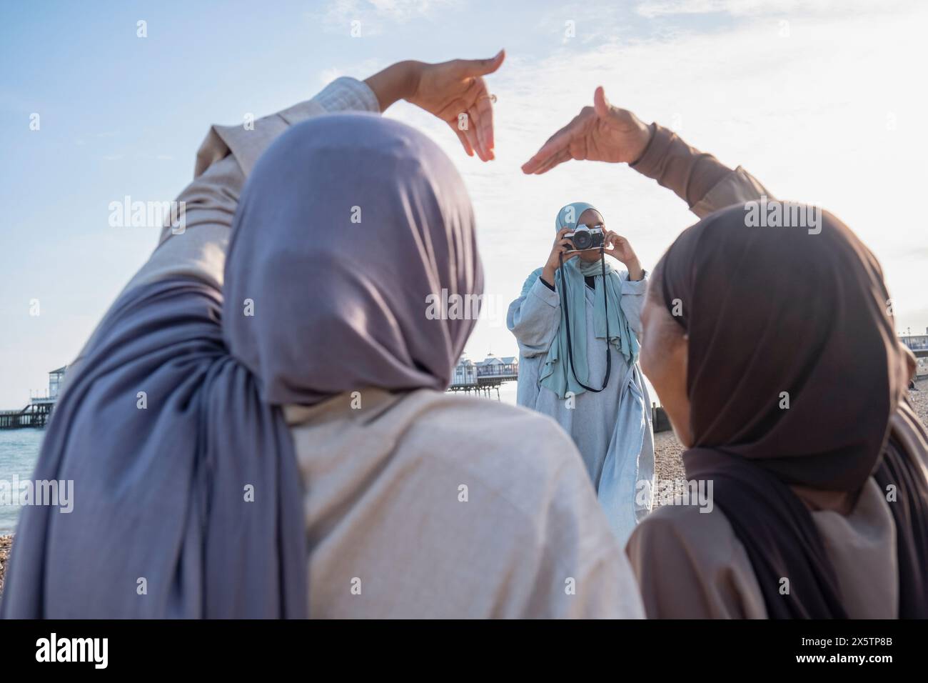 Frau, die muslimische Freunde fotografiert und mit Händen am Strand Herzform macht Stockfoto