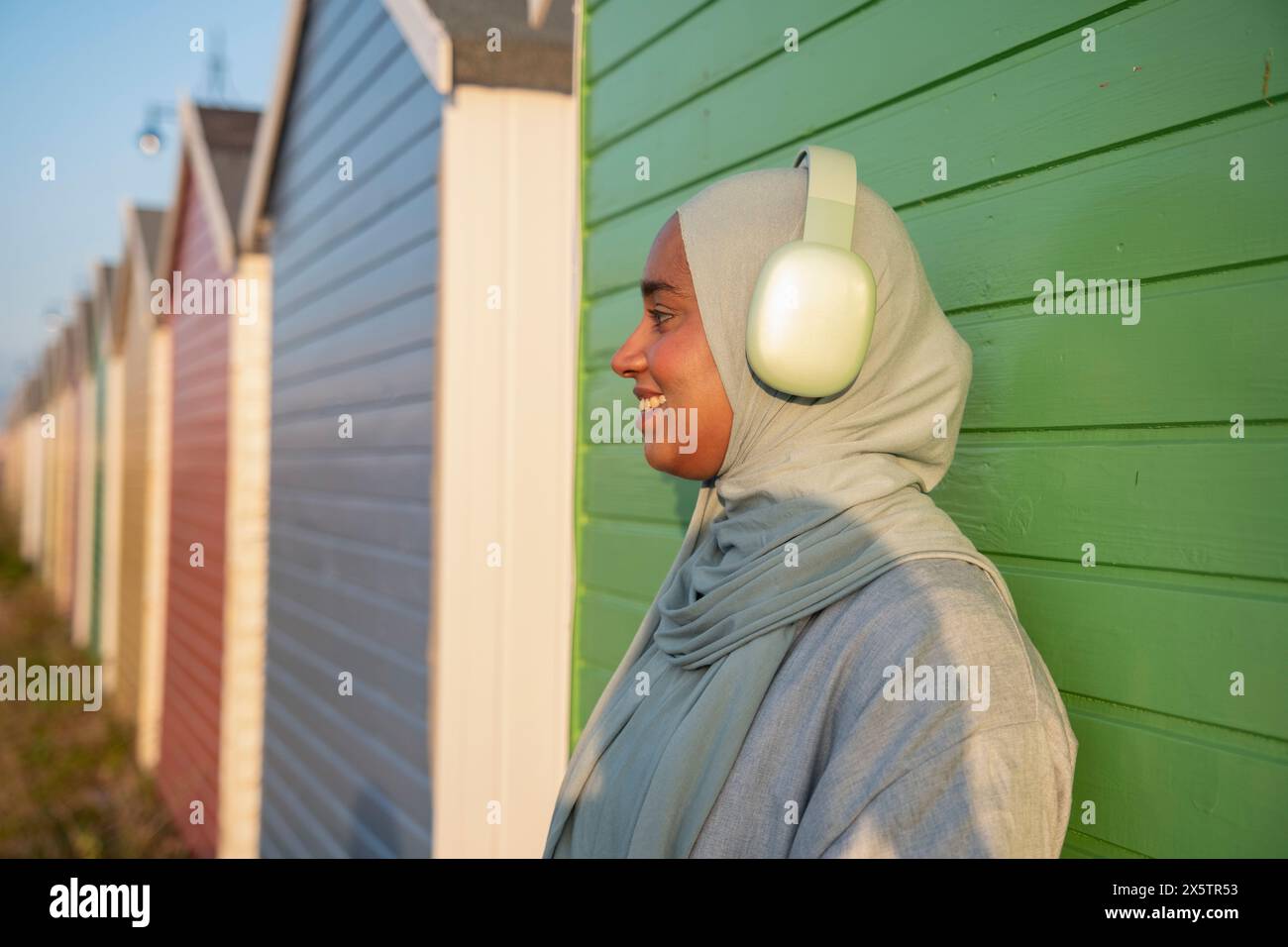 Seitenansicht einer muslimischen Frau, die am sonnigen Tag Musik hört Stockfoto