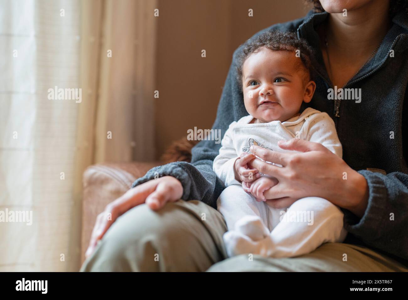 Junge Mutter, die zu Hause ein Mädchen auf dem Schoß hält Stockfoto
