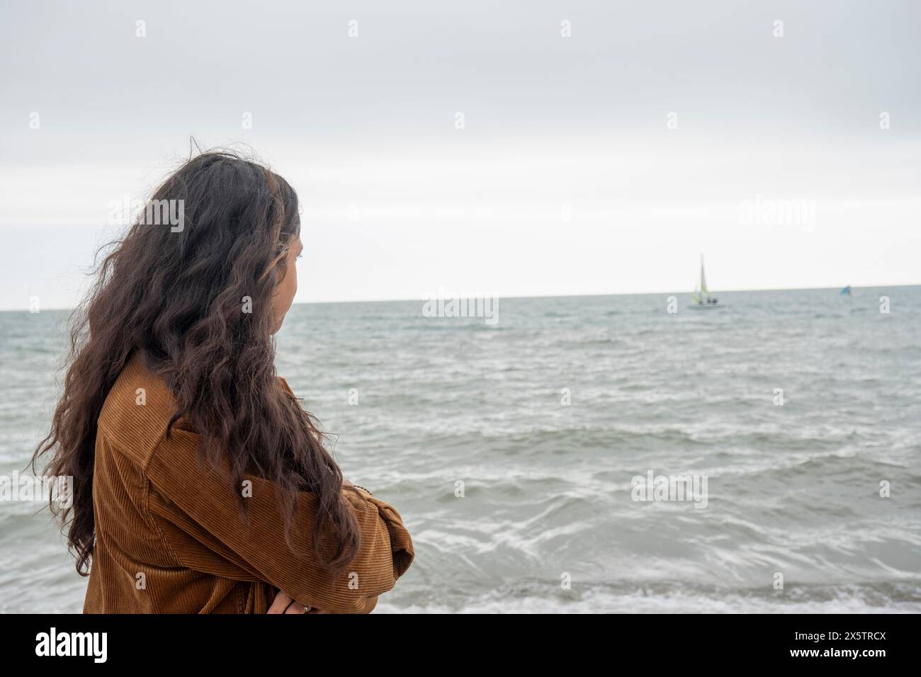 Nachdenkliche Frau, die an bewölktem Tag auf das Meer schaut Stockfoto