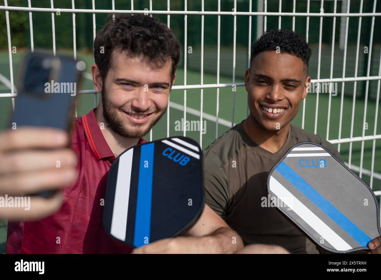 Zwei lächelnde Männer sitzen auf dem Pickleball-Platz und machen Selfie mit dem Smartphone Stockfoto