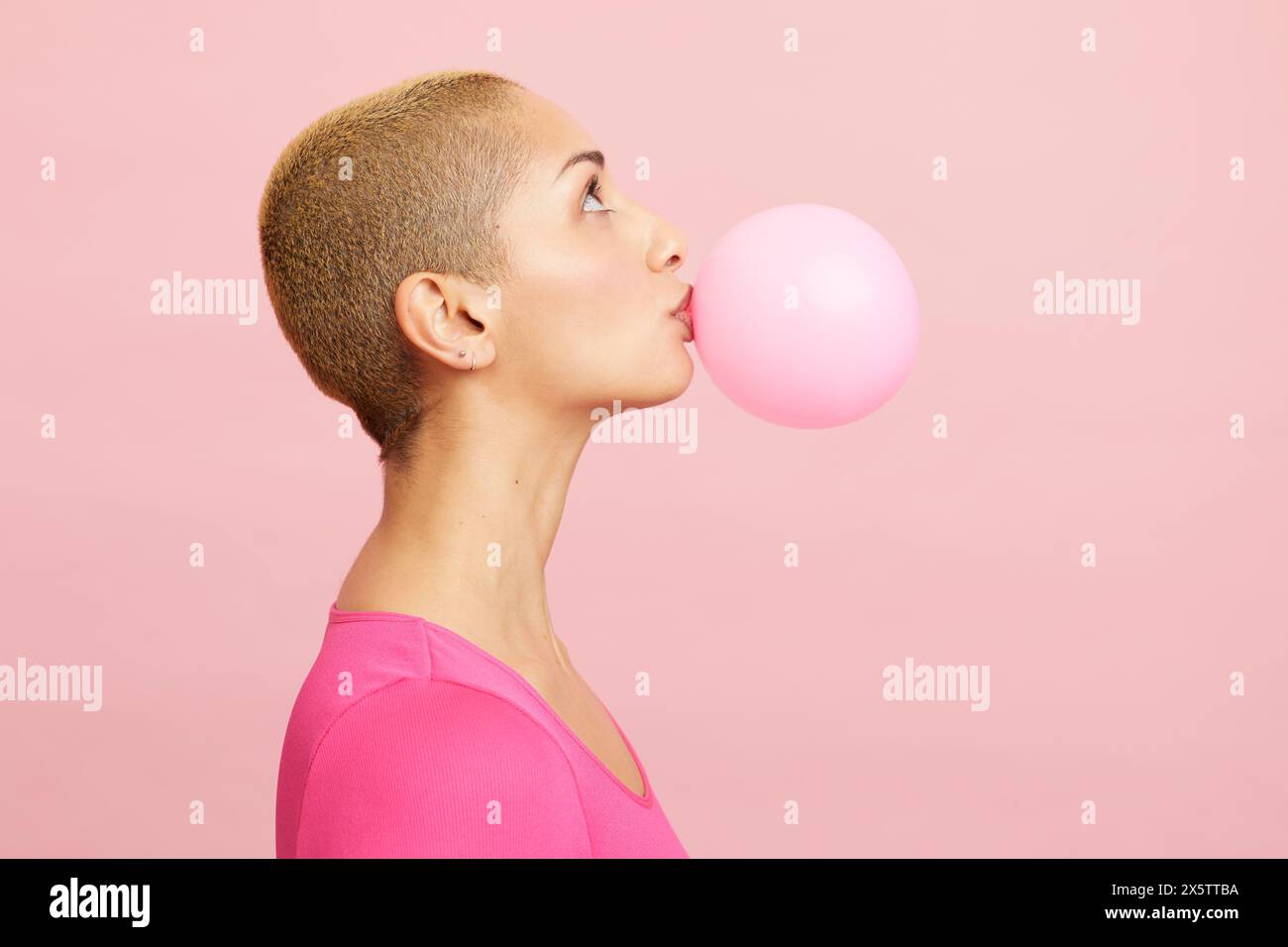 Junge blonde Frau, die einen rosafarbenen Ballon bläst Stockfoto