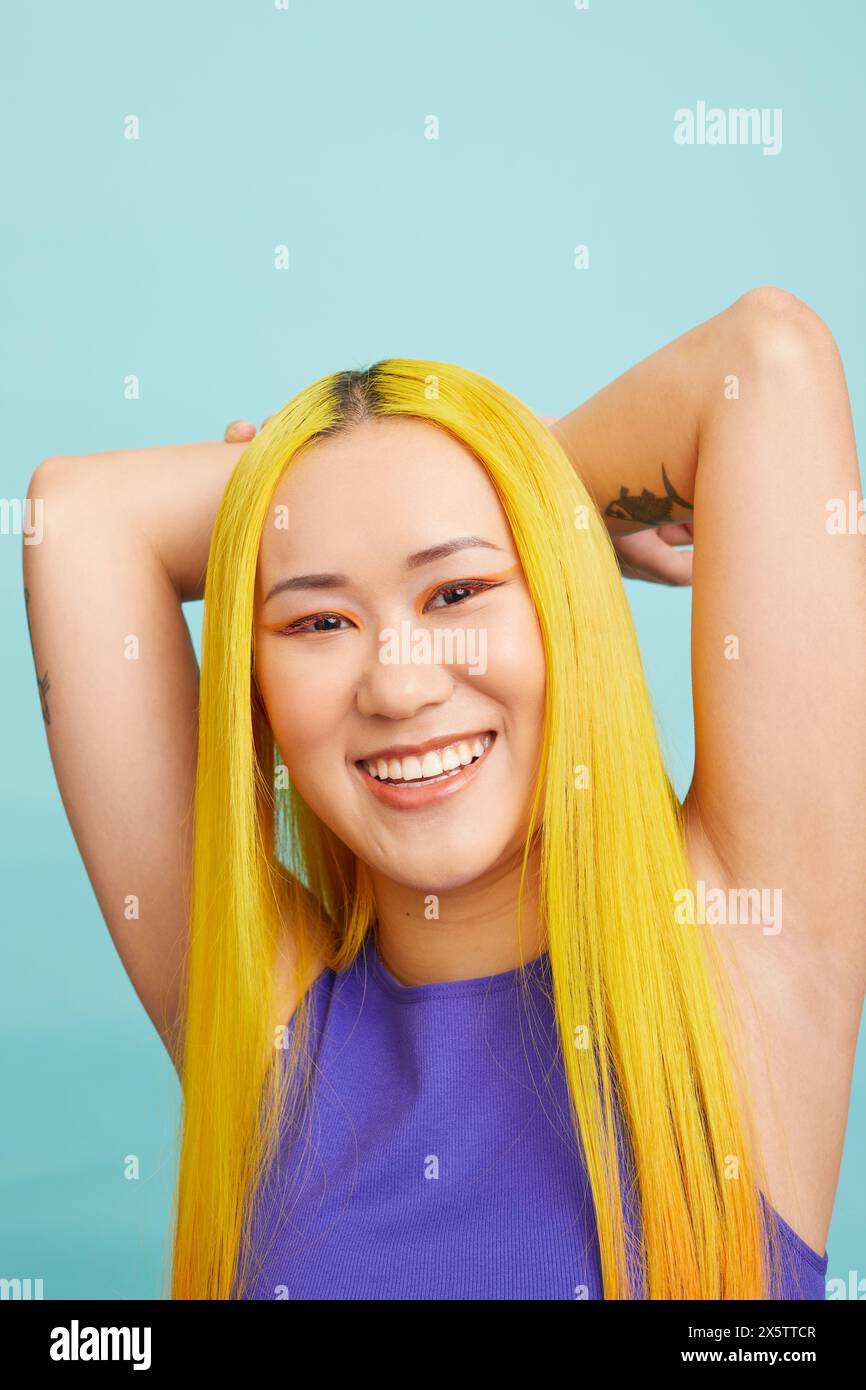 Porträt einer jungen Frau mit langen gelben Haaren, die Arme hinter dem Kopf hält Stockfoto