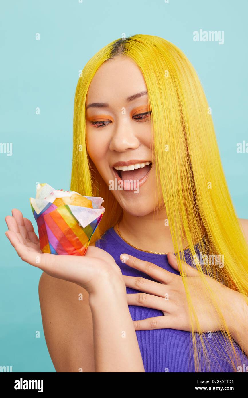 Lächelnde junge Frau mit gelbem Haar, die Tasse Kuchen hält Stockfoto