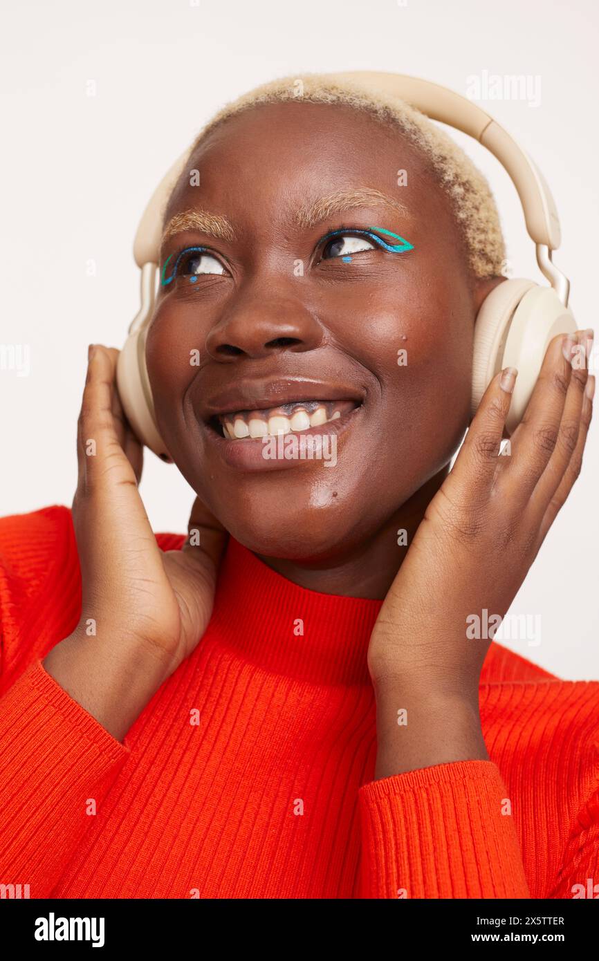 Lächelnde Frau mit kurzen weißen Haaren, die Kopfhörer trägt und Musik hört Stockfoto