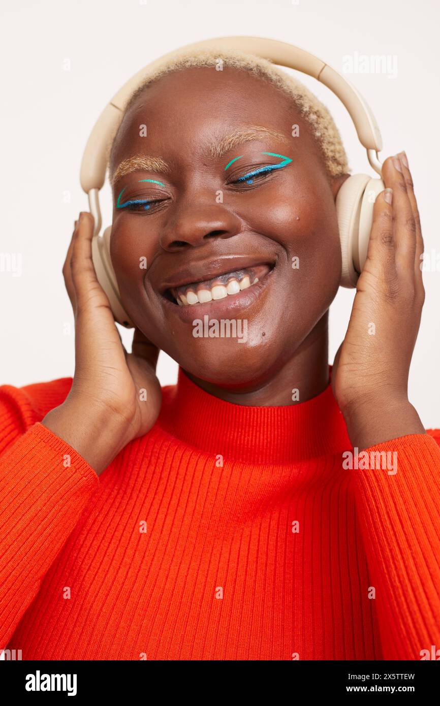 Lächelnde Frau mit kurzen weißen Haaren, die Kopfhörer trägt und Musik hört Stockfoto