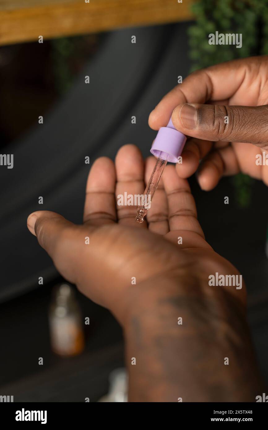 Mann, der Schönheitsprodukt mit Pipette auf die Hand aufträgt Stockfoto