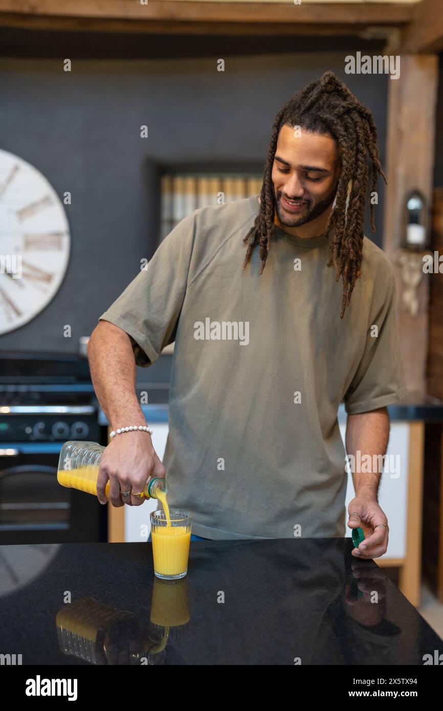 Mann mit Dreads, der Orangensaft in die Küche gießt Stockfoto