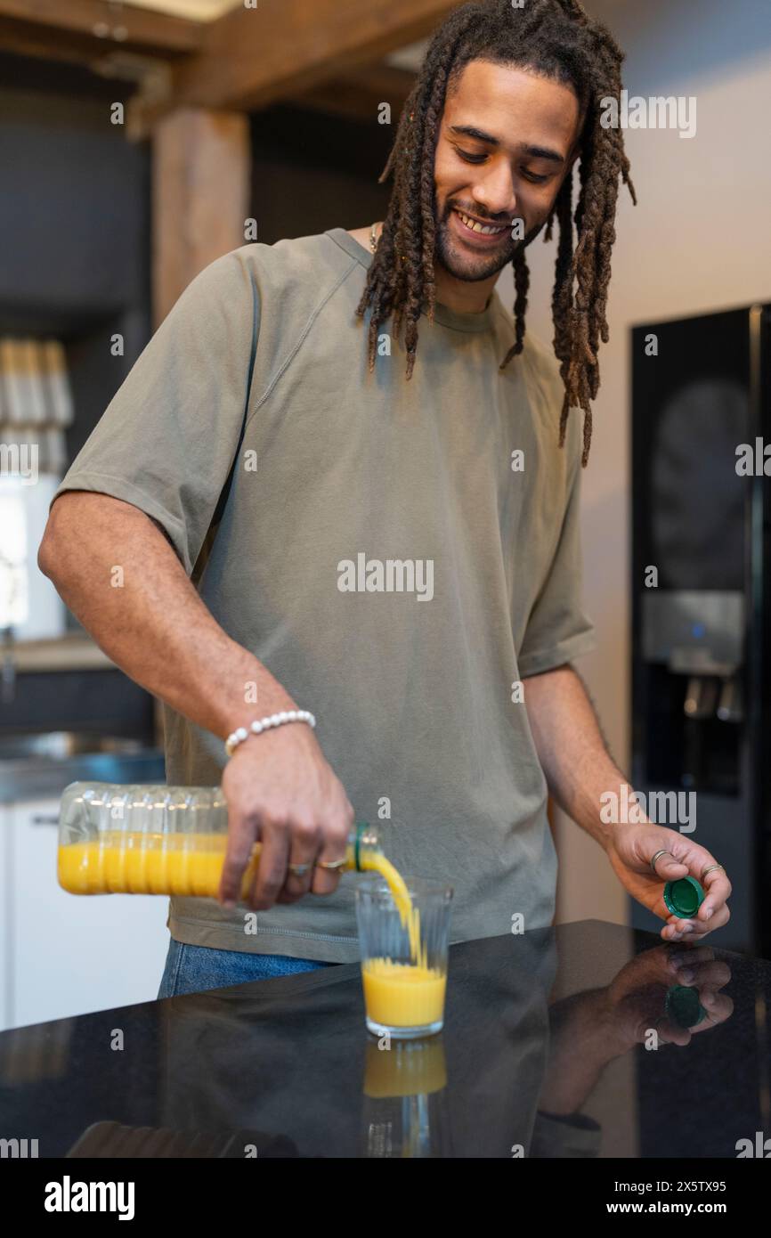 Mann mit Dreads, der Orangensaft in die Küche gießt Stockfoto
