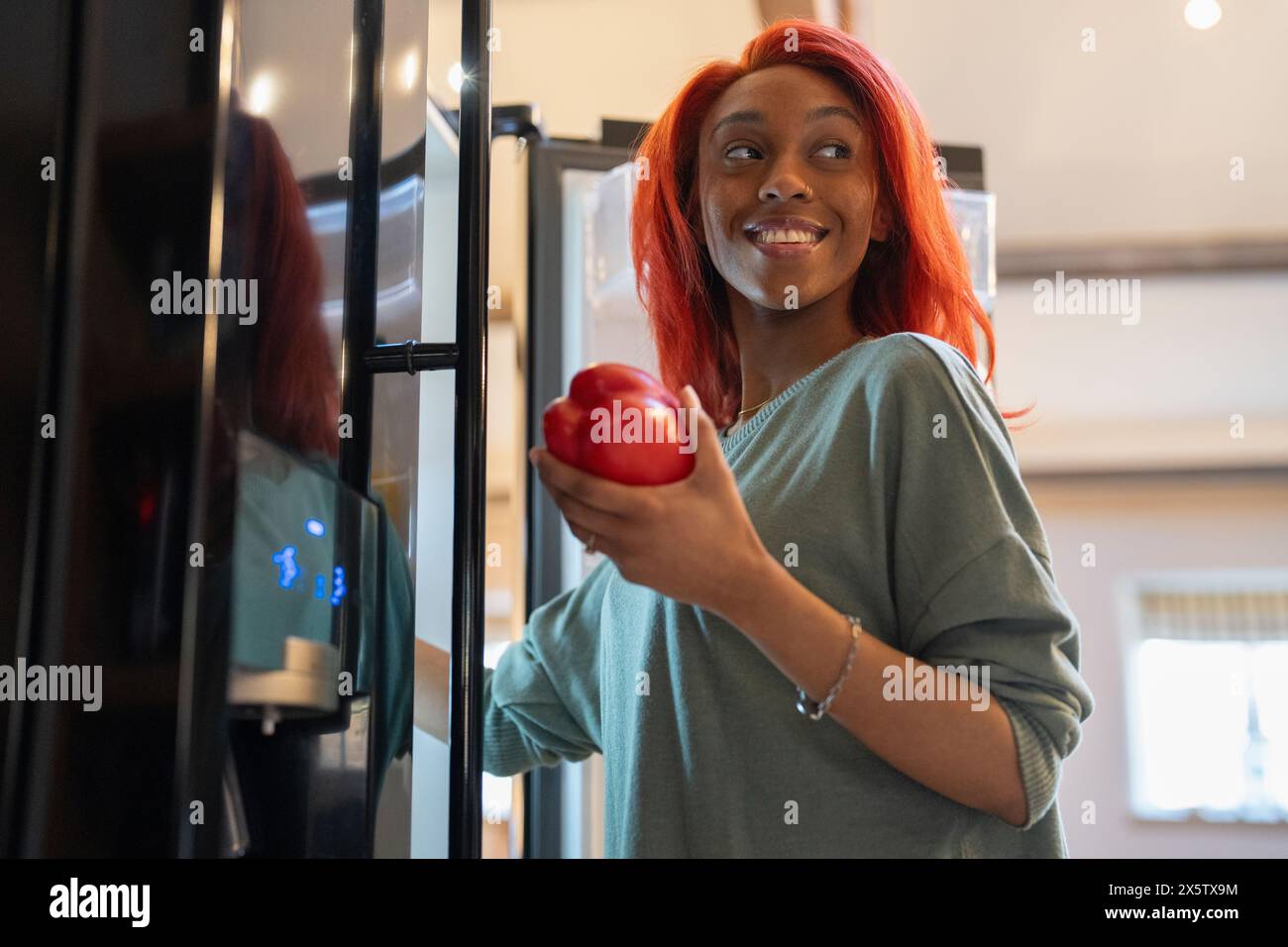 Frau, die Paprika neben dem offenen Kühlschrank hält Stockfoto