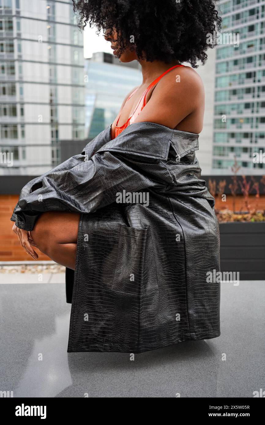 USA, Frau in schwarzem Ledermantel, die draußen hockt Stockfoto