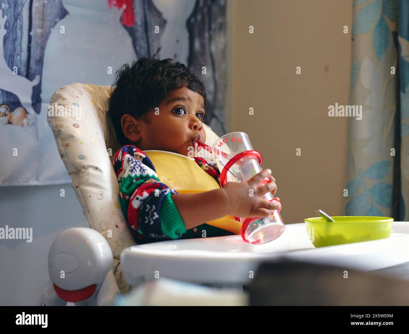 Junge sitzt im Hochstuhl und trinkt Stockfoto