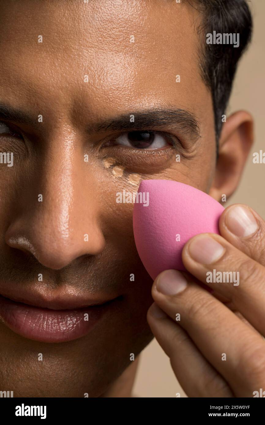 Nahaufnahme eines Mannes, der die Foundation unter dem Auge aufträgt Stockfoto