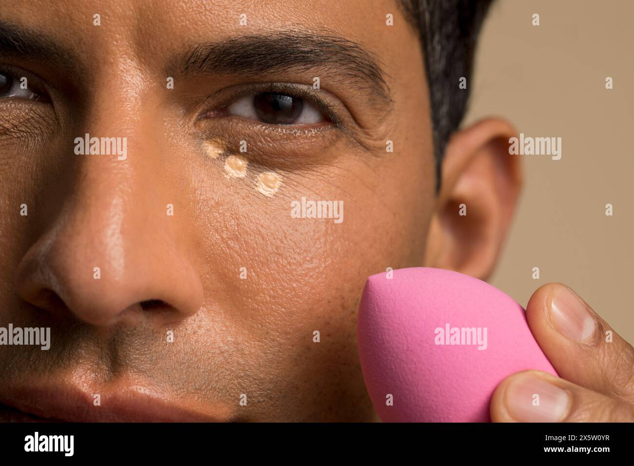 Nahaufnahme eines Mannes, der die Foundation unter dem Auge aufträgt Stockfoto