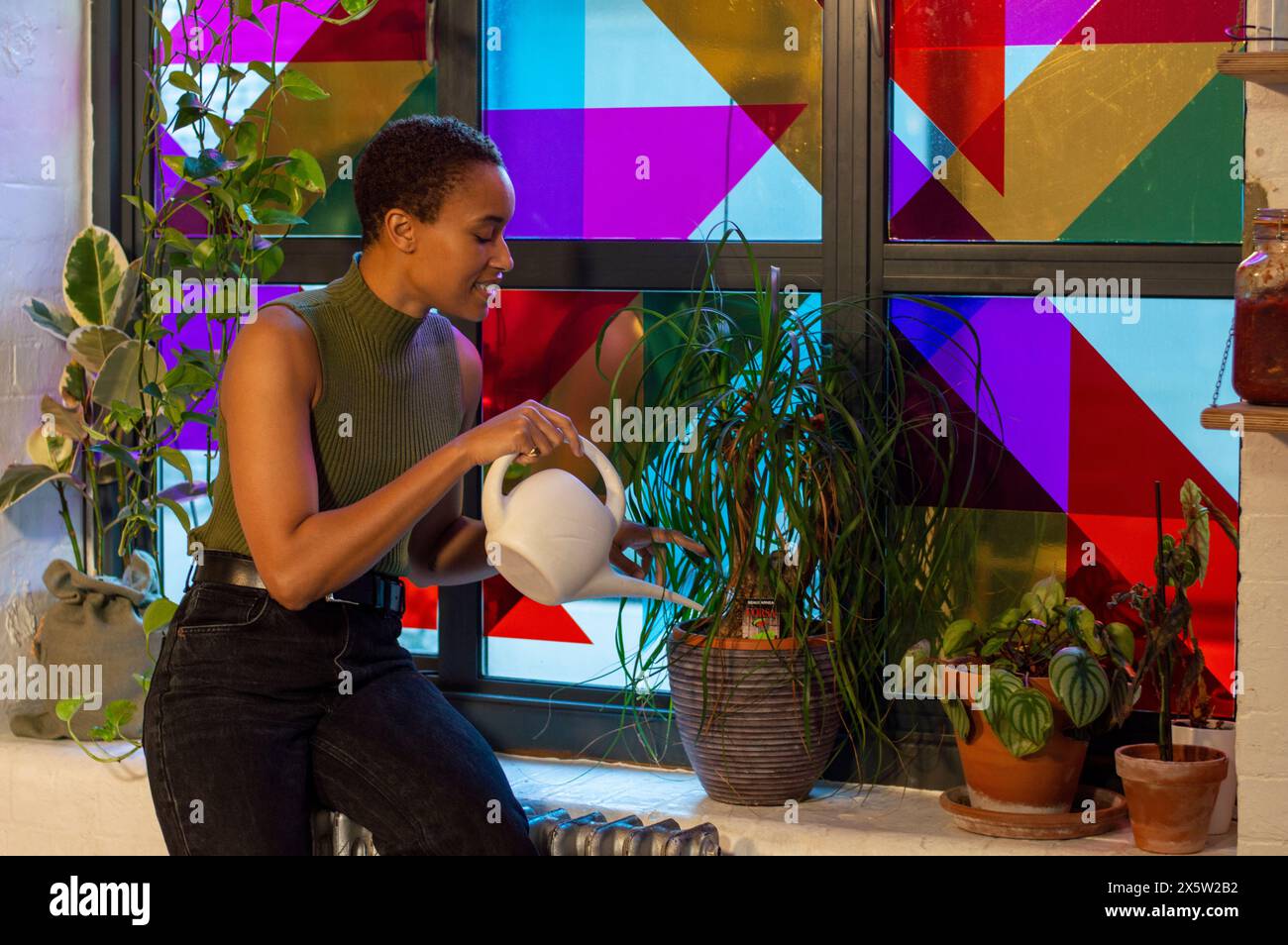 Frau, die Pflanzen an einem bunten Fenster tränkt Stockfoto