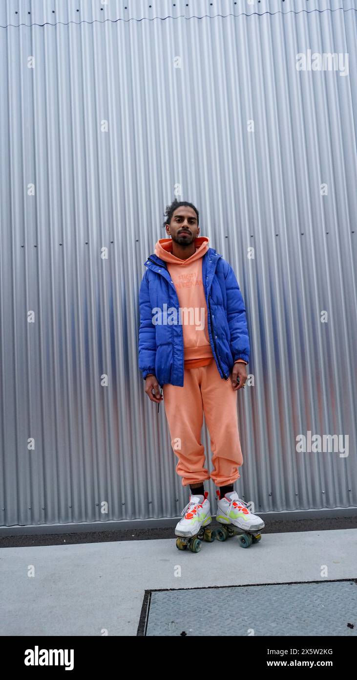 Junger Mann mit Rollschuhen, der an einer eisernen Wand steht Stockfoto