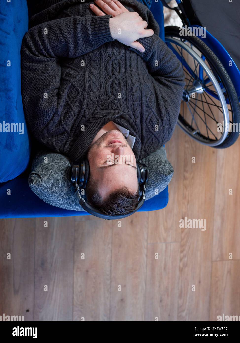 Blick von oben auf einen Mann mit Kopfhörern auf dem Sofa neben dem Rollstuhl Stockfoto