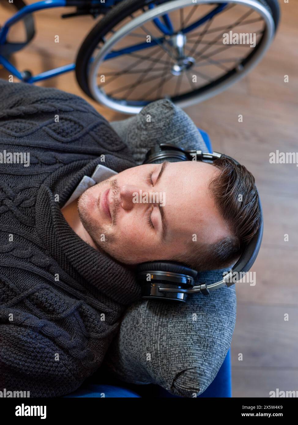 Blick von oben auf einen Mann mit Kopfhörern auf dem Sofa neben dem Rollstuhl Stockfoto