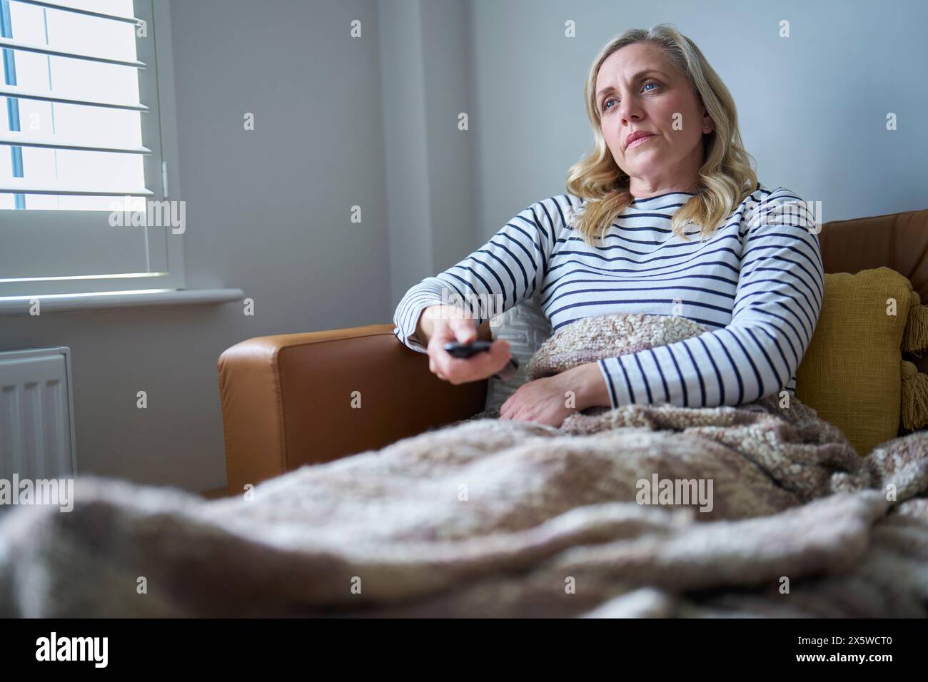 Reife wirtschaftlich inaktive Frau mit Langzeitkrankheiten auf dem Sofa zu Hause und Fernsehen Stockfoto