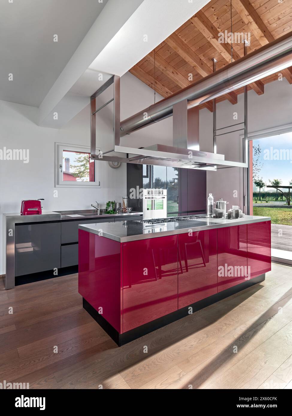 Innenausstattung einer modernen rot lackierten Küche im Vordergrund die Inselküche, der Boden ist aus Holz und die Decke ist aus freiliegenden Holzbalken Stockfoto
