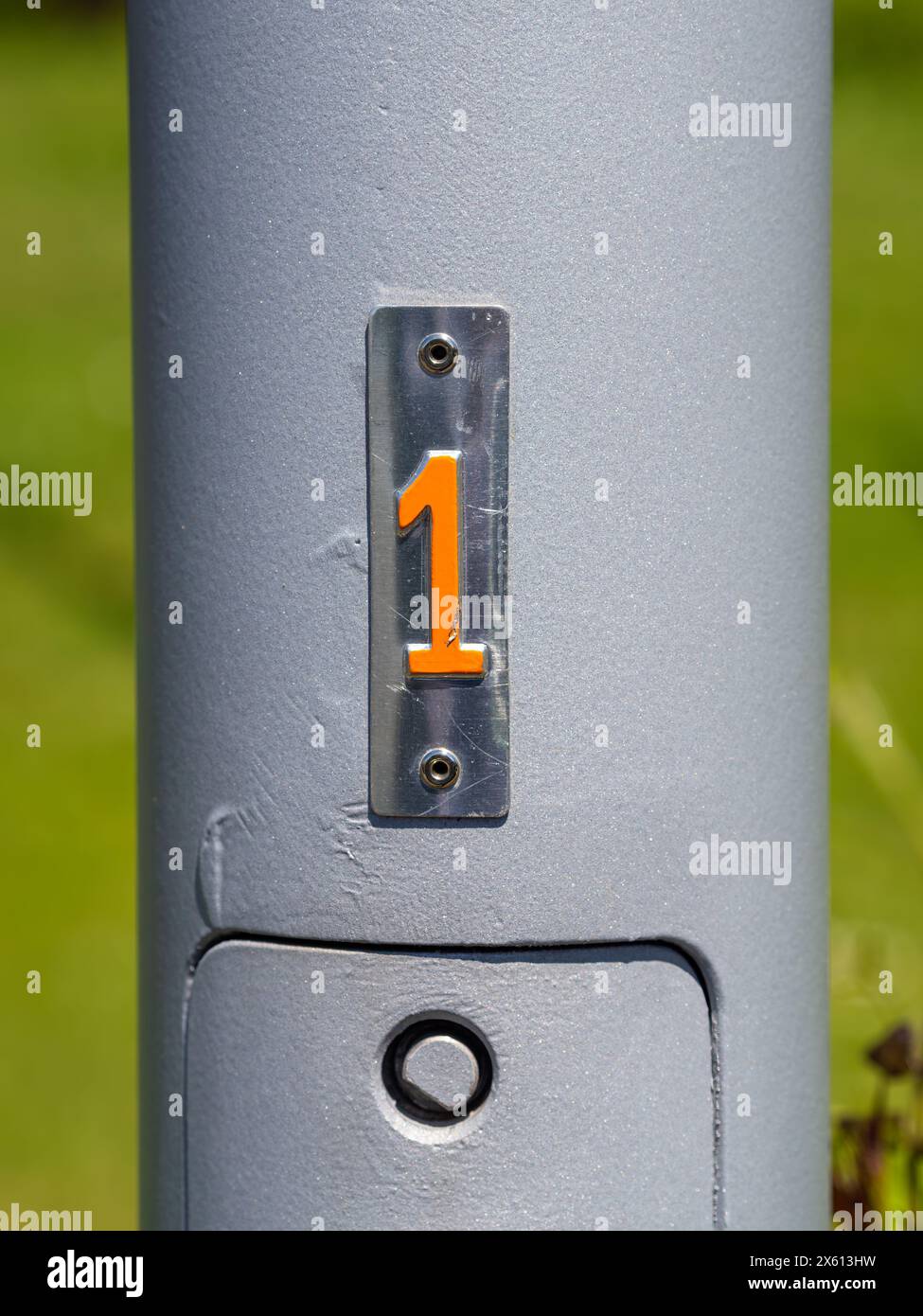 Nahaufnahme eines metallischen Stabs mit der Zahl 1 in leuchtendem Orange vor grauem Hintergrund. Stockfoto