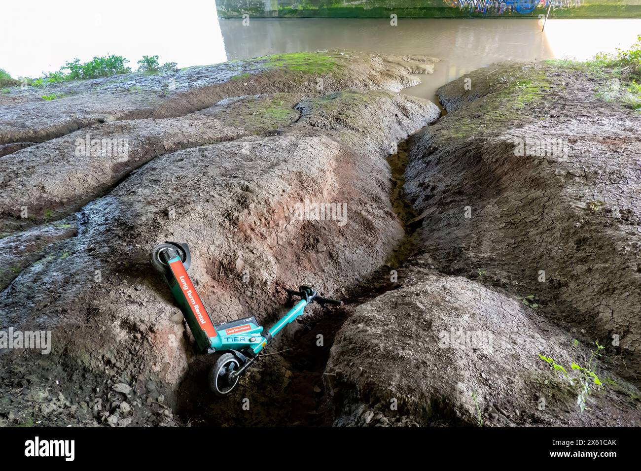 Ein mietbarer E-Scooter, der auf das schlammige Ufer des Avon in Bristol, Großbritannien, geworfen und aufgegeben wurde. Ein Beispiel für antisoziales Verhalten Stockfoto