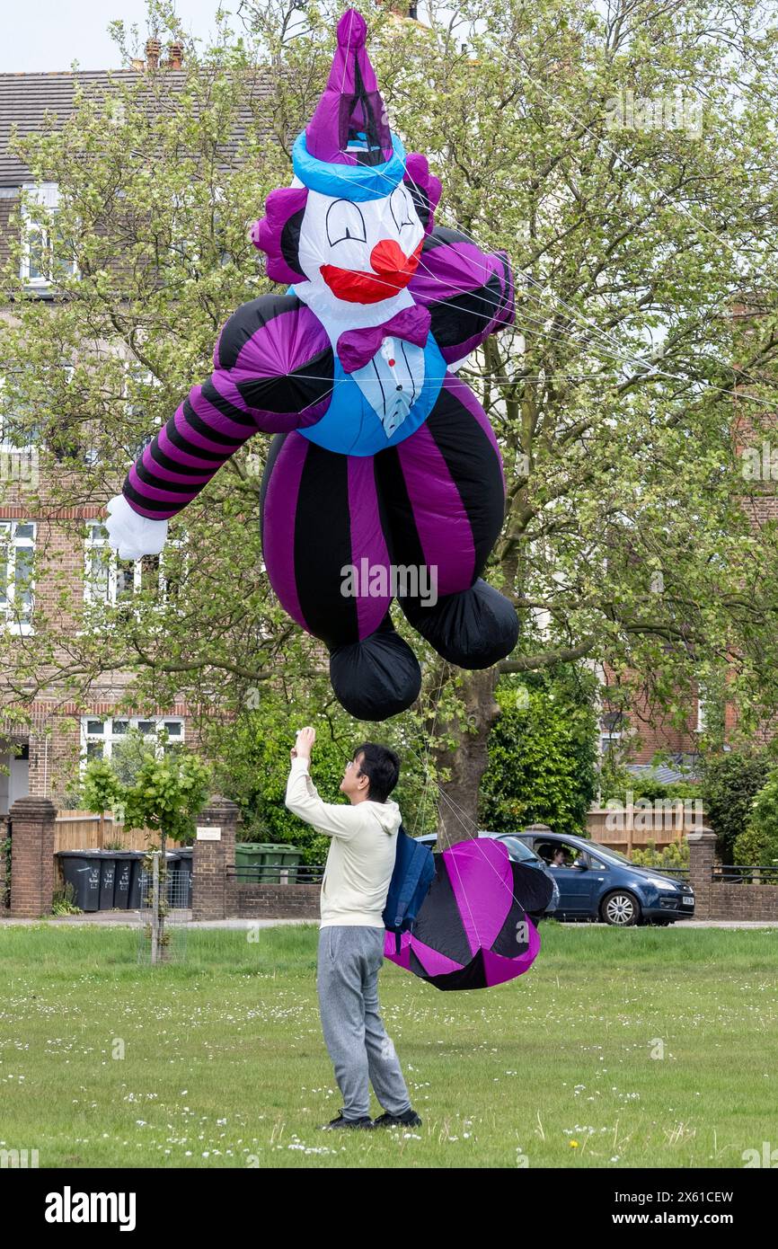 London, Großbritannien. 12. Mai 2024. Ein Mann unter einem riesigen Clowndrachen, der von Simon Hennessy von Brighton Kite Flyers geflogen wurde, als Drachenflieger am 23. Streatham Common Kite Day teilnehmen. Die beliebte Veranstaltung bringt Kite-Enthusiasten nach Streatham Common, darunter Experten und Familien, die einen Tag ausklingen möchten. Quelle: Stephen Chung / Alamy Live News Stockfoto