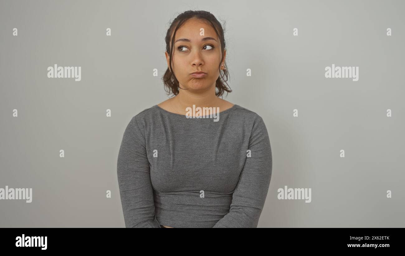 Eine junge hispanische Frau sieht vor einem isolierten weißen Hintergrund nachdenklich aus und zeigt eine lässige, aber attraktive Frisur und ein Verhalten. Stockfoto