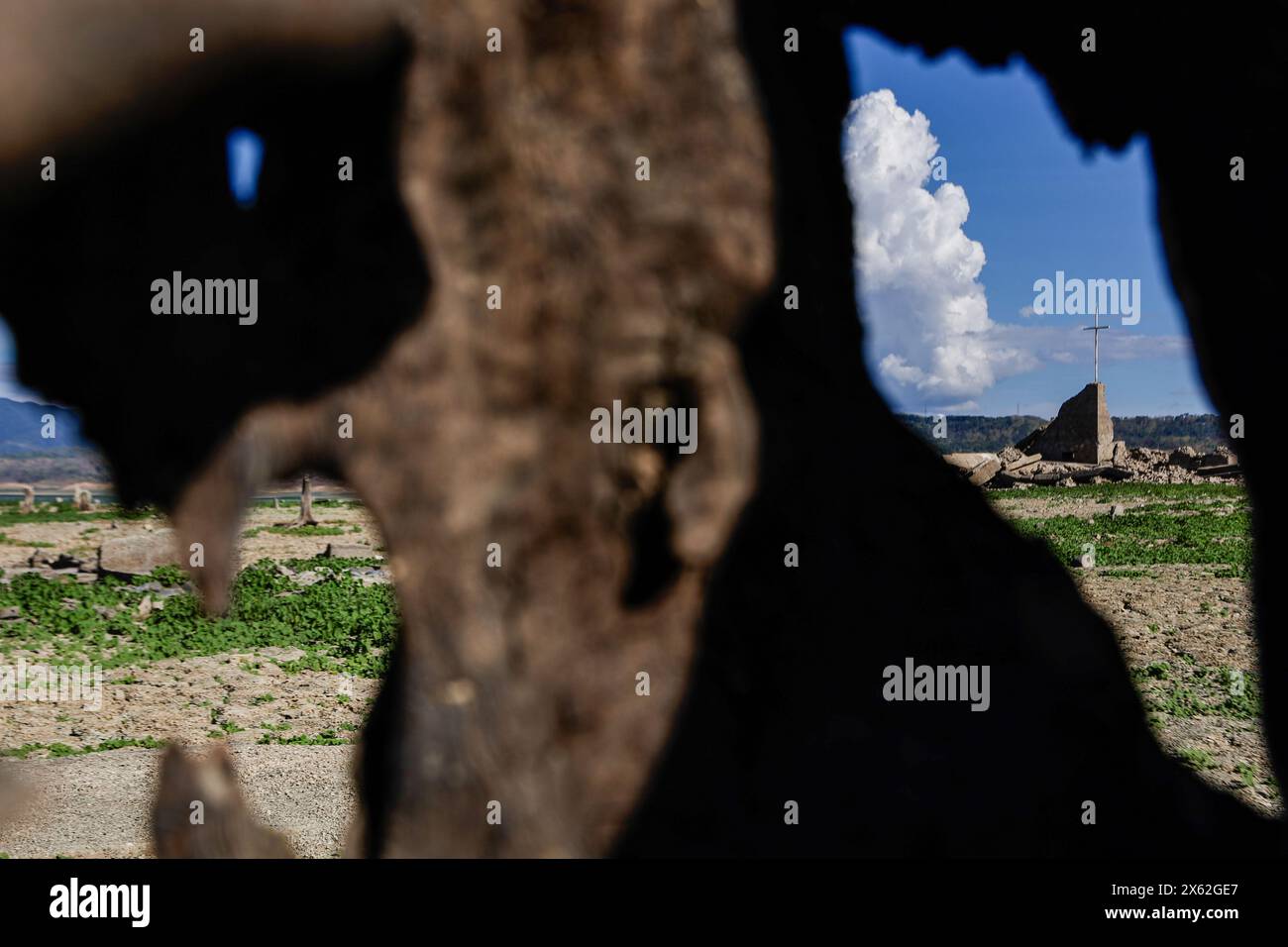 Pantabangan, Philippinen. 12. Mai 2024, Pantabangan, Philippinen: Reste der alten versunkenen Stadt Pantabangan, die wieder aufgetaucht sind, werden durch einen verwelkten Baum an einem trockenen Teil des Reservoirs gesehen, als Folge einer schweren Dürre aufgrund der steigenden Temperaturen auf den Philippinen. Das sechste Wiederauftauchen dieser 300 Jahre alten Siedlung, die eine Kirche und mehrere Grabsteine umfasst, hat Touristen zu Besuch gezogen, nachdem der Wasserstand am Damm aufgrund der El Nino Klimabildungen gesunken ist. Quelle: ZUMA Press, Inc./Alamy Live News Stockfoto