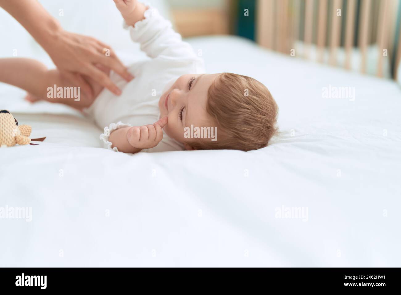 Entzückendes Kleinkind lächelt selbstbewusst auf dem Bett und liegt mit der Puppe im Schlafzimmer Stockfoto