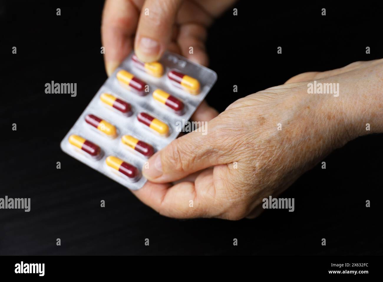 Pillen in faltigen Händen älterer Frauen auf dunklem Holztischhintergrund. Medikation in Kapseln, Einnahme von Beruhigungsmitteln, Antibiotika oder Vitaminen im Alter Stockfoto