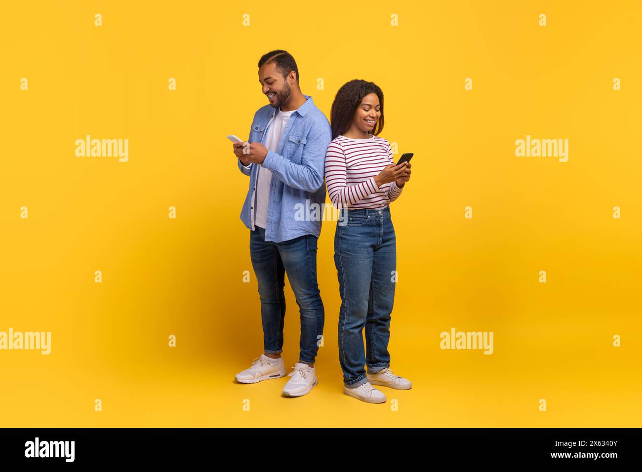 Zwei Personen stehen mit Smartphones vor gelbem Hintergrund hintereinander Stockfoto