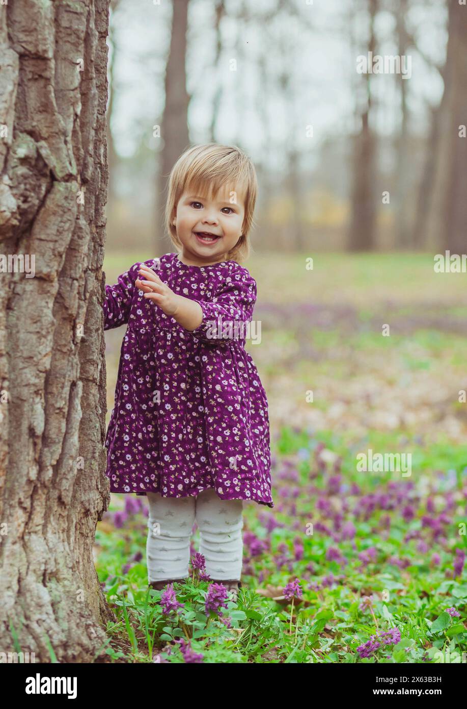 Blondes Baby in einem farbigen Kleid, das auf einer Waldlude mit Blumen läuft Stockfoto