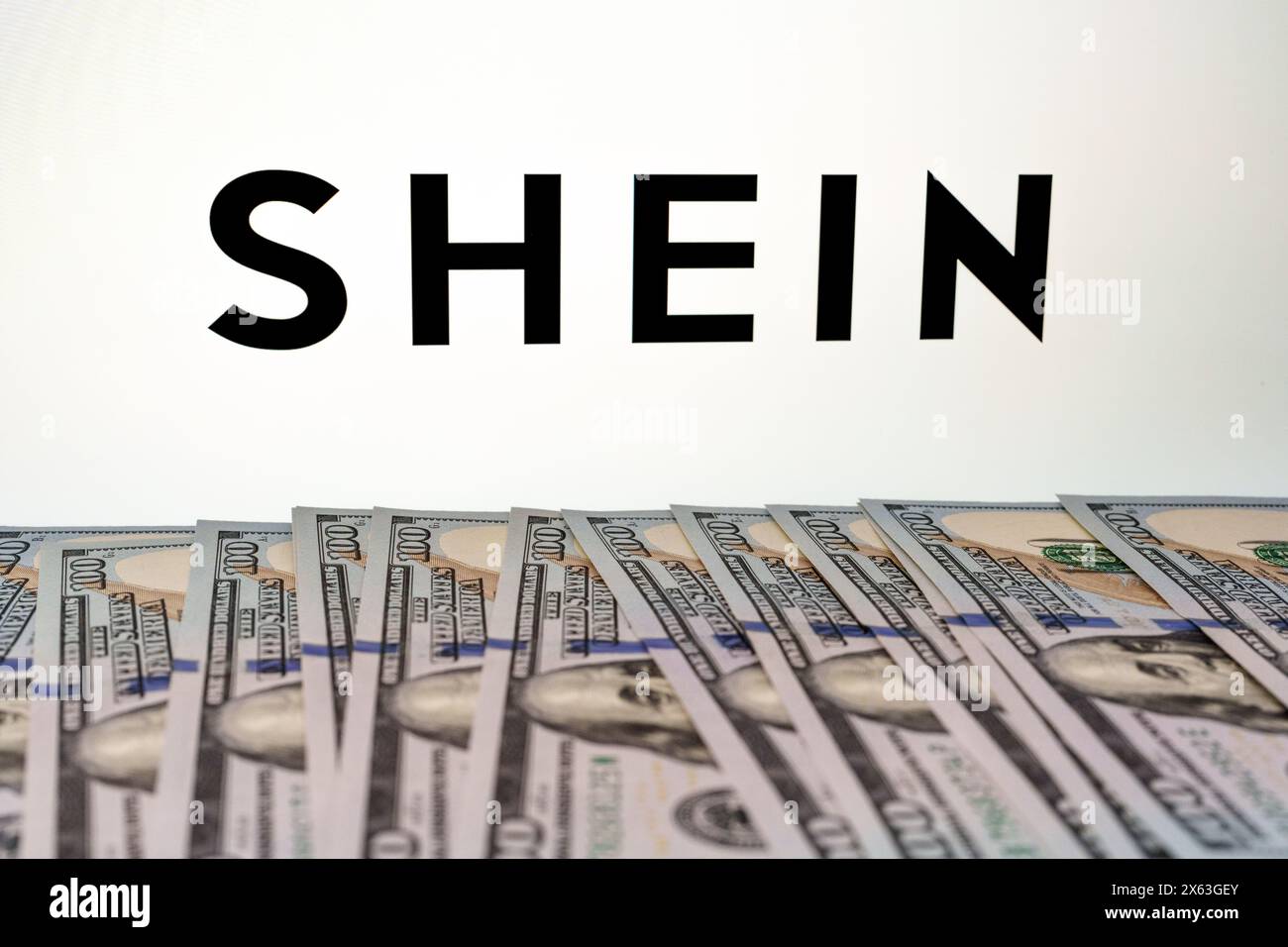 SHEIN Logo auf dem Bildschirm und Dollarscheine in der Nähe. Stafford, Vereinigtes Königreich, 28. April 2024 Stockfoto