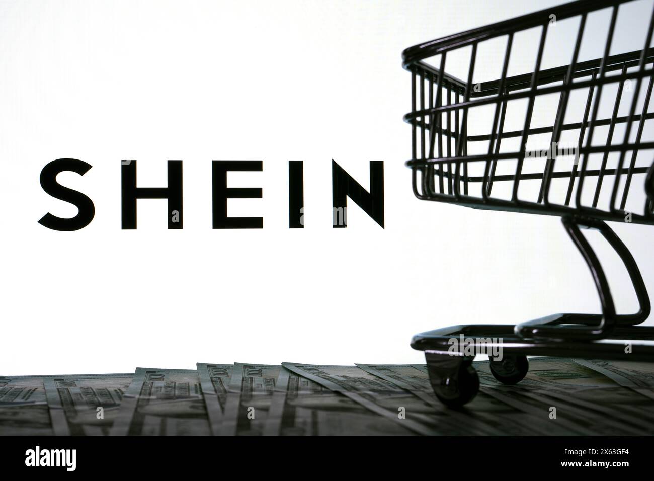 SHEIN Logo auf dem Bildschirm neben Dollar-Banknoten und Mini-Einkaufswagen. Stafford, Vereinigtes Königreich, 28. April 2024 Stockfoto