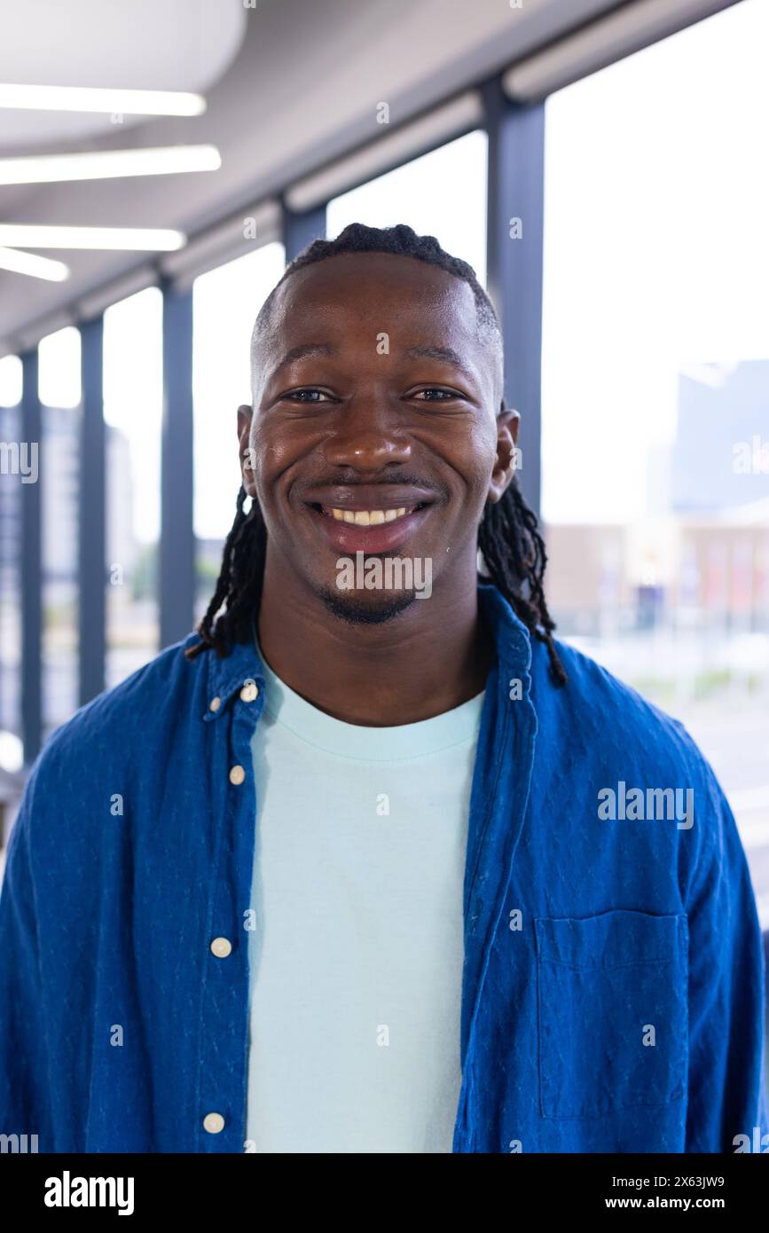 Im modernen Büro, junger afroamerikanischer Mann in lässiger Kleidung, der hell lächelt Stockfoto