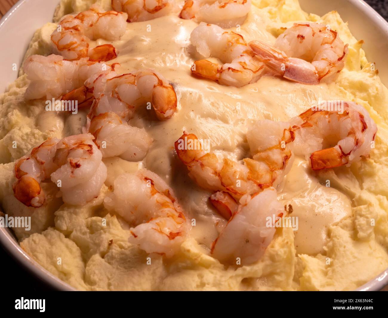 Eine Nahaufnahme eines Fischauflaufes, in dem die reichhaltige Konsistenz von Kartoffelpüree im Kontrast zu prallen Garnelen in einem cremigen Weißwein präsentiert wird Stockfoto