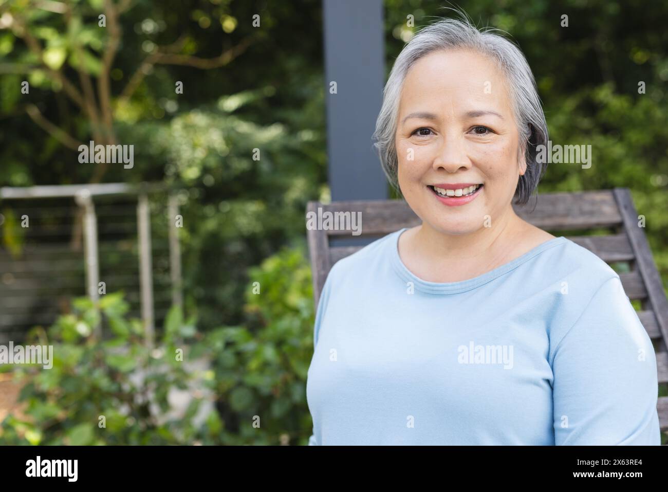 Draußen lächelt eine ältere asiatische Frau, sitzt mit hellblauem Hintergrund, Kopierraum Stockfoto