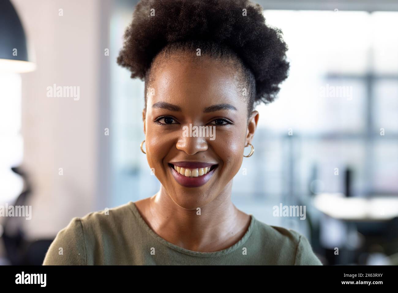 Im Büro lächelt eine afroamerikanische Geschäftsfrau, die lässige Kleidung trägt Stockfoto