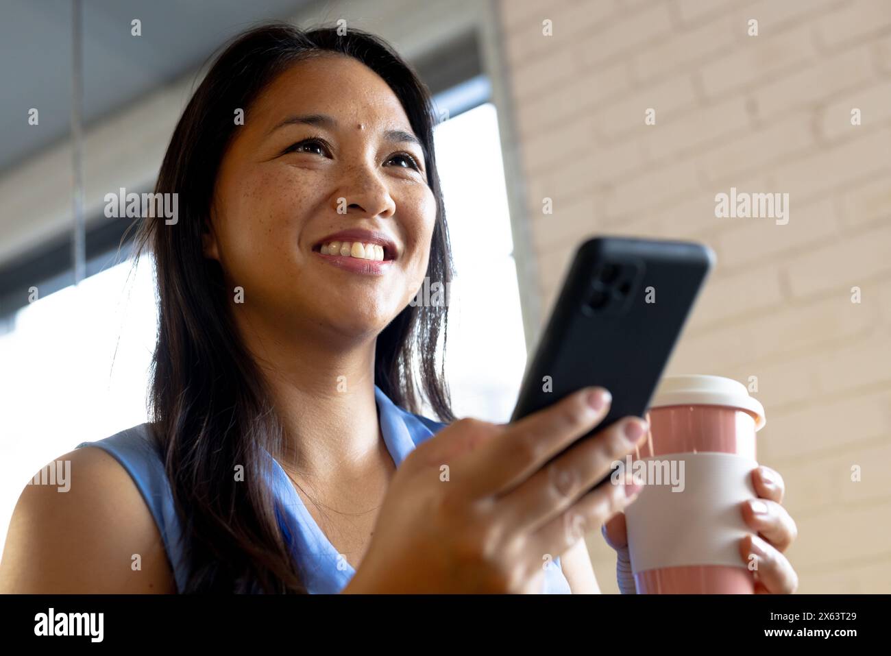 Im Büro, eine Geschäftsfrau, die ein Smartphone hält und wegschaut Stockfoto