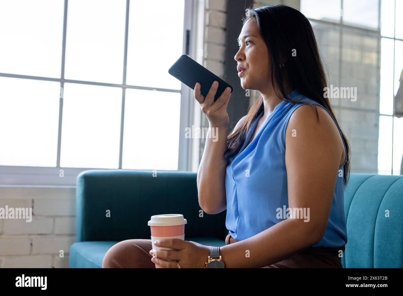 Im Büro, eine Geschäftsfrau, die ein Smartphone hält und wegschaut Stockfoto
