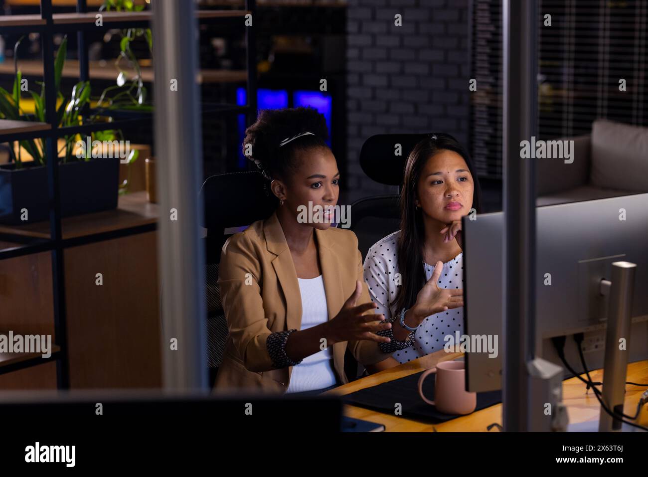 Im Büro diskutieren verschiedene weibliche Geschäftskollegen über Computer, arbeiten bis spät Stockfoto