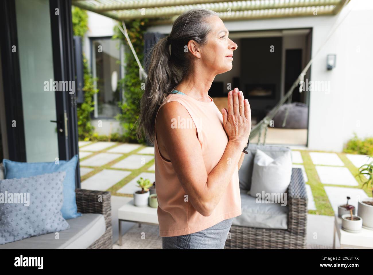 Zu Hause steht eine reife weiße Frau draußen, Hände zusammen, macht Yoga Stockfoto